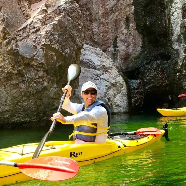 People kayaking in yellow boats on green water near rocky cliffs.