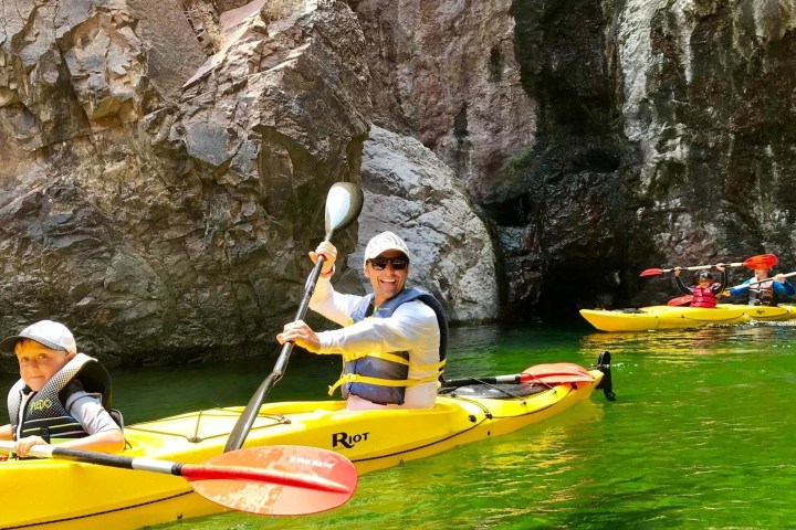People kayaking through rocky canyon with green water.