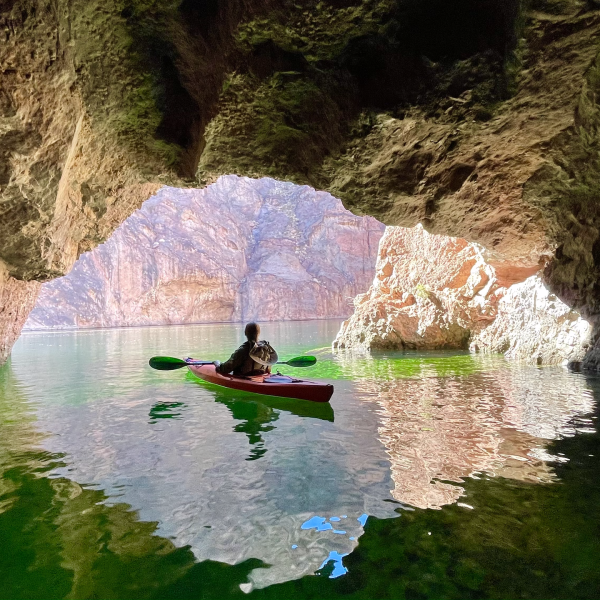 Person kayaking in a cave with sunlight reflecting on water.