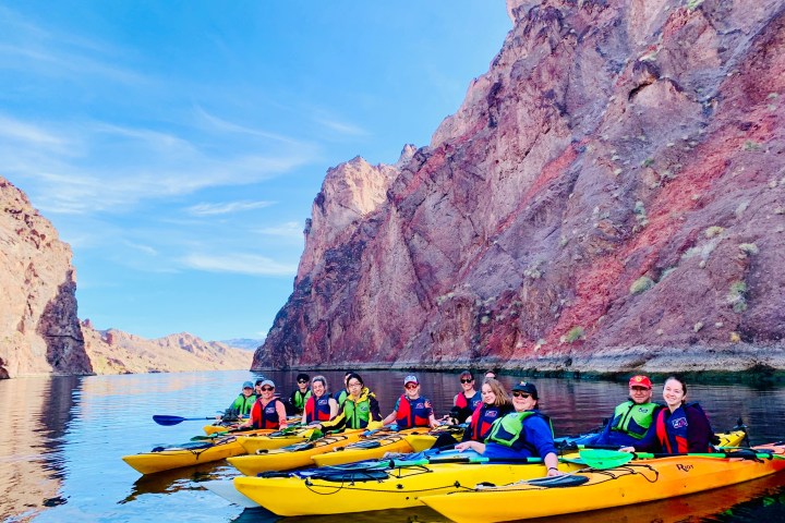Group kayaking in yellow kayaks on a river between rocky cliffs.