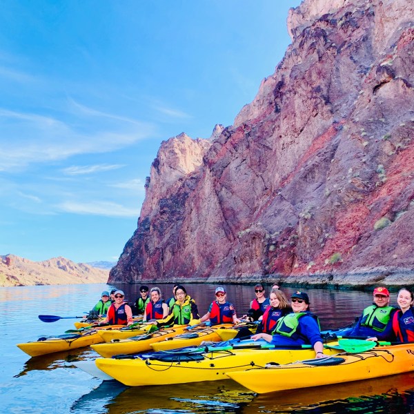 Group kayaking in yellow kayaks between rocky cliffs on calm water.