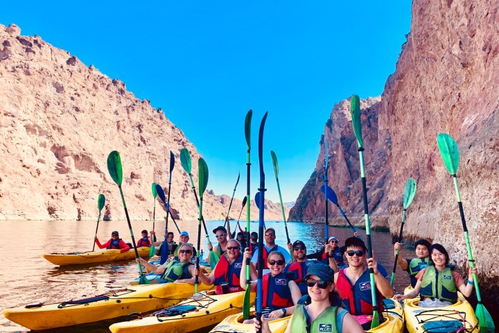 Group of people kayaking in a canyon with blue sky above.