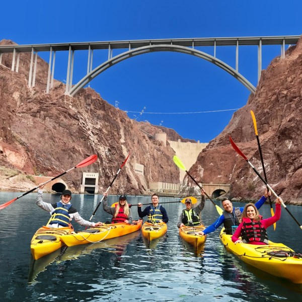 Group kayaking under a large bridge in a canyon.