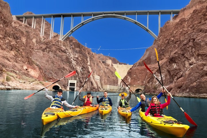 Group kayaking under a large bridge in a canyon.