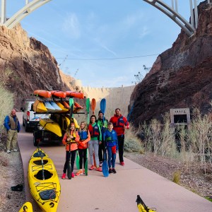 Group with kayaks under large bridge at canyon location.