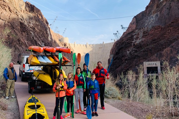 Group with kayaks under large bridge at canyon location.
