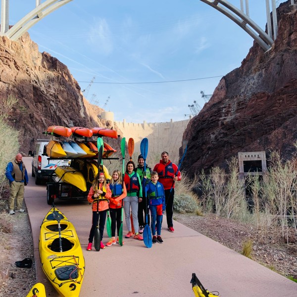 Group with kayaks under a large bridge and a dam in the background.