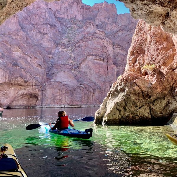 Kayakers exploring a cave with rocky walls and clear water.