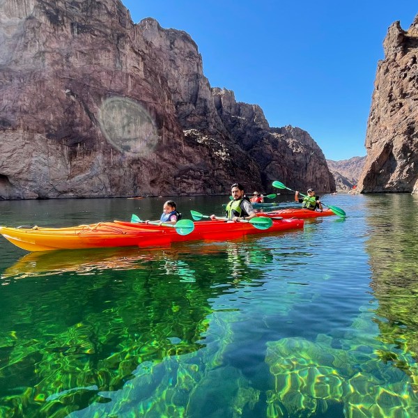People kayaking on clear green water between rocky cliffs.