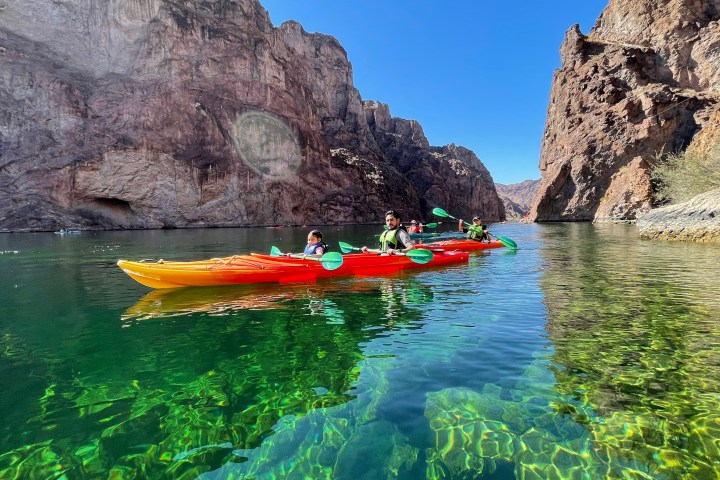 People kayaking on clear green water between rocky cliffs.