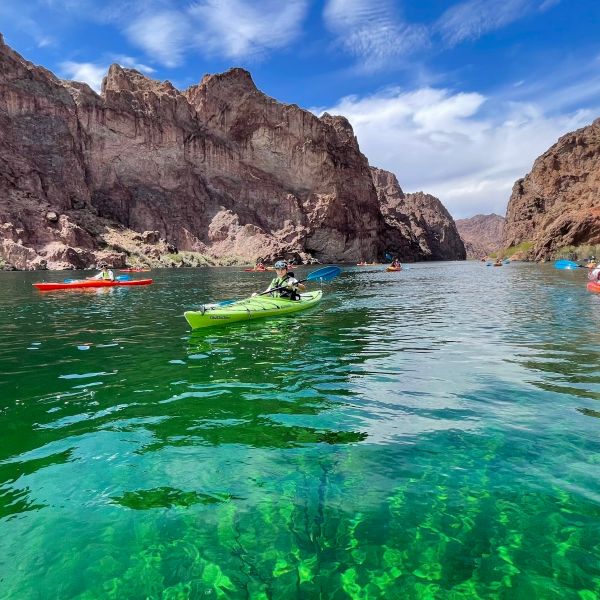 Kayakers on a clear green river surrounded by rocky cliffs under a blue sky.