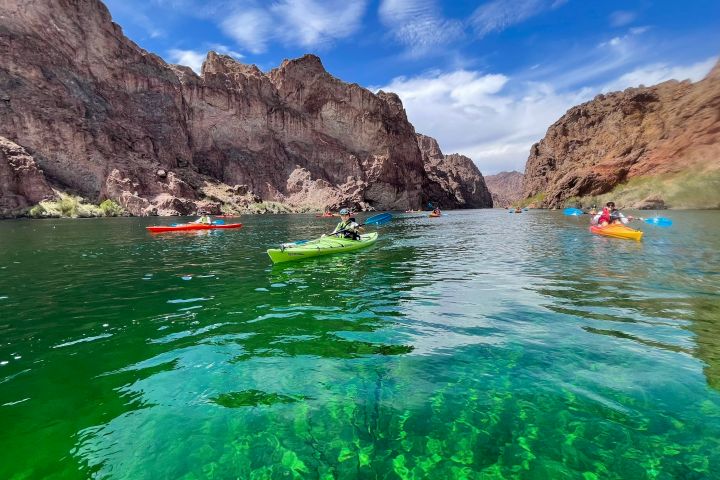 Kayakers on a clear green river surrounded by rocky cliffs under a blue sky.