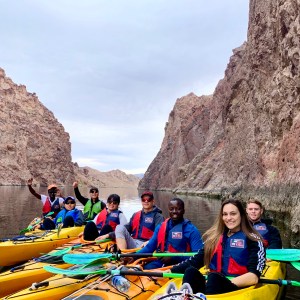 Group of people kayaking between tall canyon walls on a calm river.