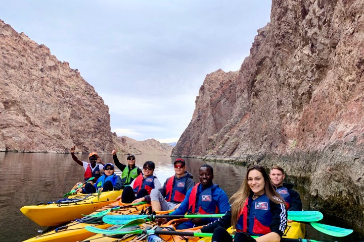 Group of people kayaking between tall canyon walls on a calm river.