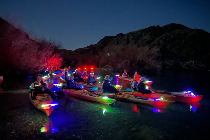 Group in kayaks with colorful lights on a river at night.