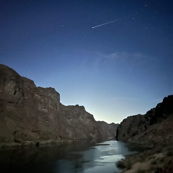 Night sky with shooting star over rocky canyon and river