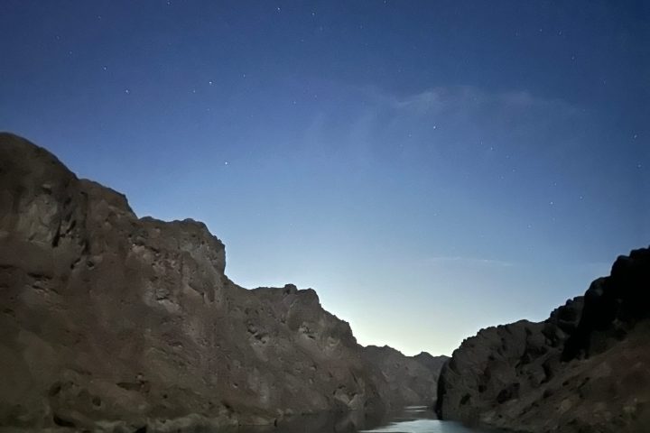 Night sky with shooting star over rocky canyon and river