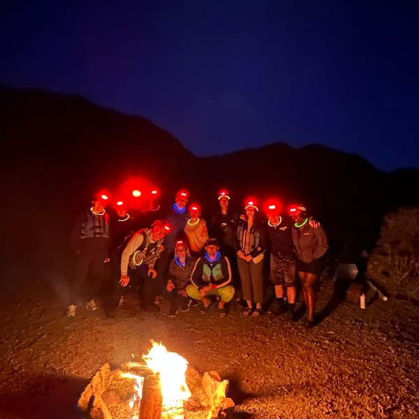 Group with headlamps around campfire at night under moon.