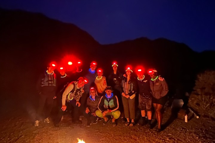 Group with headlamps around a campfire under a moonlit sky.