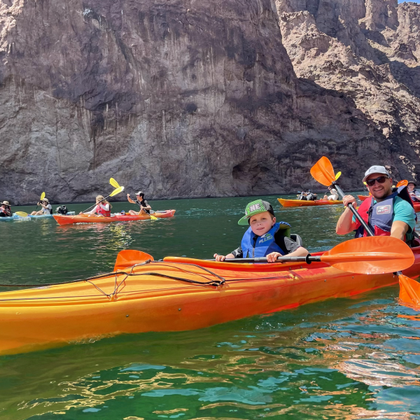 People kayaking on a clear lake surrounded by rocky cliffs.
