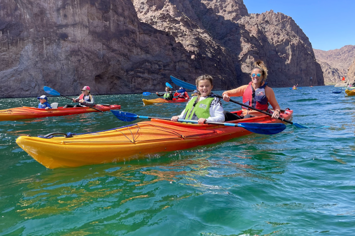 People kayaking on a river surrounded by rocky cliffs.