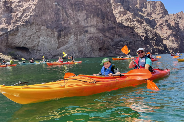 Group of kayakers paddling near rocky cliffs on a calm lake.