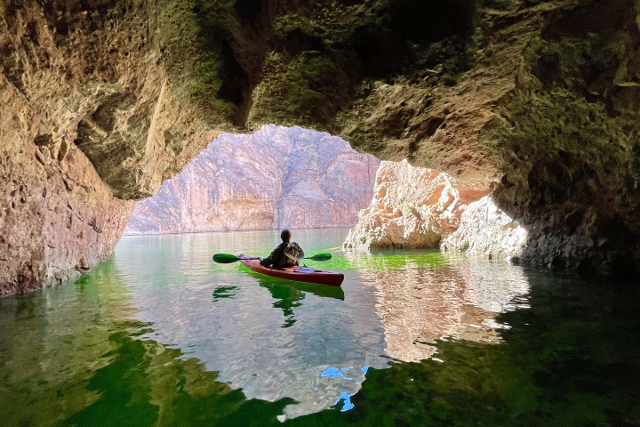 Person kayaking in cave with rocky walls and sunlit water.