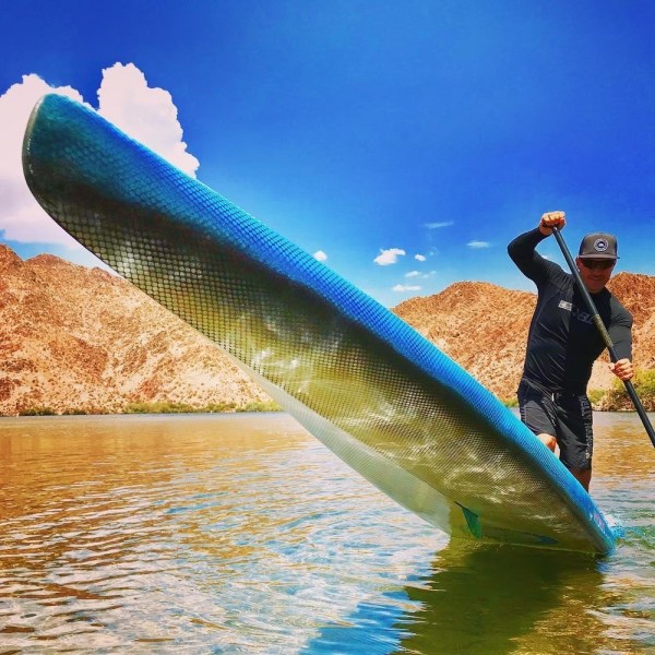 Person paddleboarding on a lake with mountains and blue sky in background.