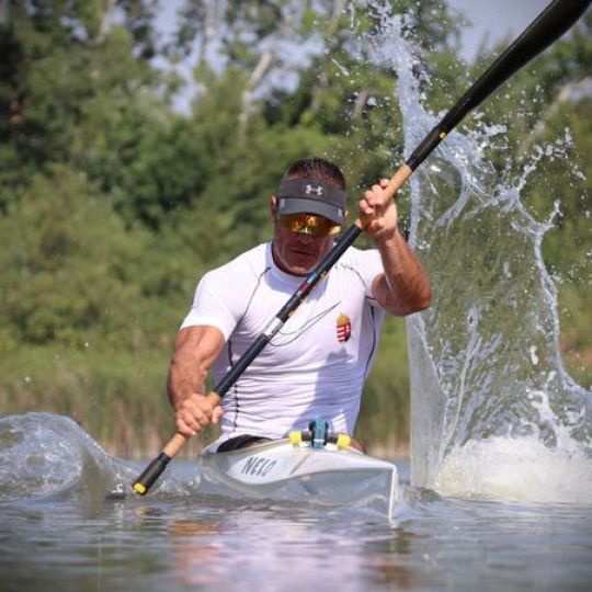 Man kayaking energetically on a lake with splashing water.