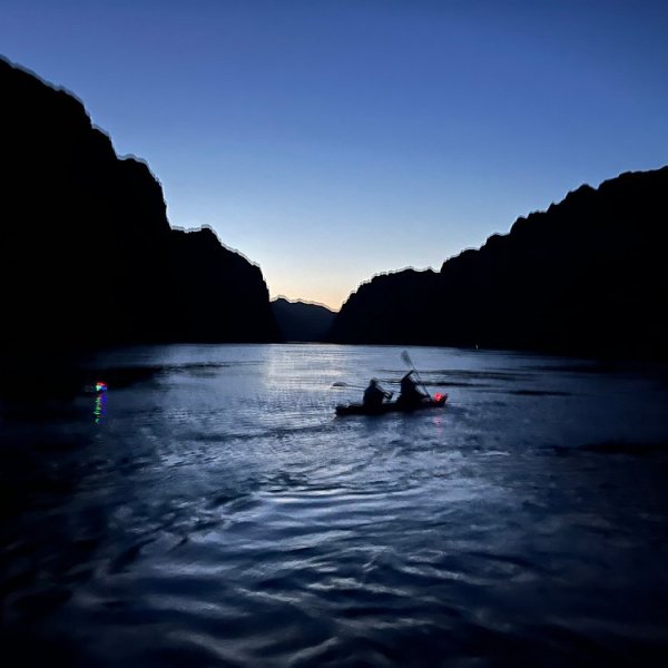 Silhouetted kayaker on calm water at dusk between dark mountains.