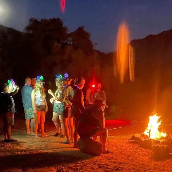 Group with glow sticks around campfire under moonlit night sky.